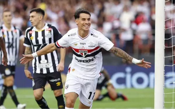 Jogador do São Paulo com a camisa número 11 corre em direção à torcida comemorando um gol, com os braços abertos e um sorriso no rosto. Atrás dele, jogadores do Santos aparecem cabisbaixos.