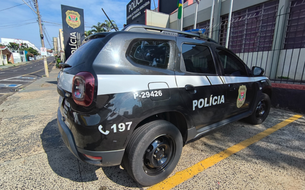 Viatura preta e branca da Polícia Civil de São Paulo estacionada em frente à Central de Polícia Judiciária (CPJ) de Franca, durante o dia. O veículo tem o número de identificação P-29426 e o telefone de emergência 197 estampados na lateral traseira. Ao fundo, é possível ver o prédio da CPJ com a bandeira do Brasil hasteada.