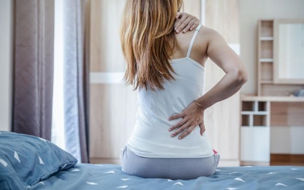 Mulher de costaqs com uma mão no ombro e outra na cintura