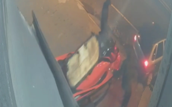 Imagem de uma câmera de segurança que mostra a ação de criminosos durante a madrugada. No canto inferior direito, aparece parcialmente um jet ski (moto aquática) vermelho preso a uma carretinha, sendo puxado por um carro prata. Um dos suspeitos, em pé ao lado do equipamento, parece finalizar a amarração antes da fuga. A cena ocorre na calçada, em frente à loja invadida, com pouca iluminação.