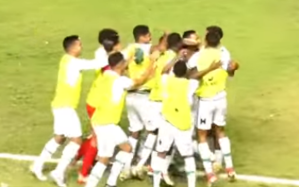 Grupo de jogadores da Francana comemora intensamente um gol dentro de campo. Todos vestem uniforme branco com coletes amarelos de treino. Eles estão abraçados, pulando e celebrando juntos, demonstrando união e entusiasmo. A cena acontece em um gramado iluminado à noite.