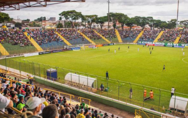 Imagem mostra o Estádio Municipal Dr. José Lancha Filho, conhecido como Lanchão, em Franca (SP). As arquibancadas estão cheias de torcedores acompanhando uma partida de futebol. O gramado aparece bem cuidado, com jogadores distribuídos em campo. O público veste em sua maioria roupas coloridas, muitos de verde e amarelo, e observa atentamente o jogo.
