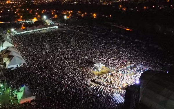 Imagem aérea noturna mostra uma multidão reunida no Parque de Exposições “Fernando Costa”, em Franca, durante uma edição do Hallel. O palco iluminado está posicionado à direita, enquanto milhares de pessoas se espalham pelo espaço aberto, formando um grande mar de fiéis. Ao fundo, as luzes da cidade completam o cenário.