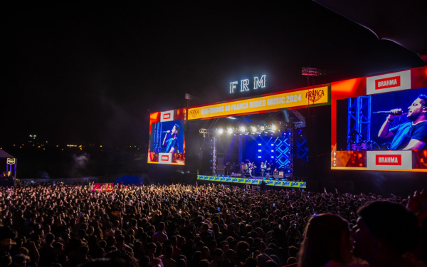 Foto noturna de um grande show no palco principal do Franca Rodeo Music. O espaço está lotado de pessoas, com uma multidão acompanhando a apresentação. O palco é iluminado com luzes coloridas, telões gigantes exibem o cantor que se apresenta e, na parte superior, há a sigla “FRM” em destaque.
